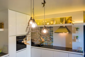 Una cocina moderna con armarios blancos, horno integrado y una lámpara de metal original.