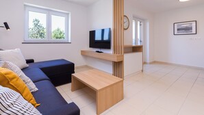 Ein modernes Wohnzimmer mit einem dunkelgrauen Sofa, einem Holztisch, einem Flachbildfernseher und einer Holzvertäfelung.
