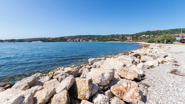 Eine felsige Küstenlinie mit freiem Blick auf das Meer und eine ferne Stadt.