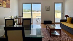 A modern living room with a glass dining table, a sofa, and a balcony with a view of the countryside. - OCEAN TERRACE HOUSE by Azores HomeMade (Ribeira Grande)