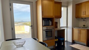 A kitchen with wooden cabinets, a microwave, an oven, and a sink. There is a table with a metal bowl and chairs. - OCEAN TERRACE HOUSE by Azores HomeMade (Ribeira Grande)