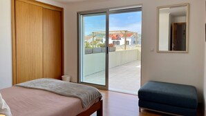 A bedroom with a bed, a bench, a sliding glass door to a balcony, and a wooden wardrobe. - OCEAN TERRACE HOUSE by Azores HomeMade (Ribeira Grande)