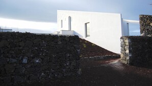 Un edificio moderno con fachada blanca, un muro de piedra en primer plano y cielo despejado.