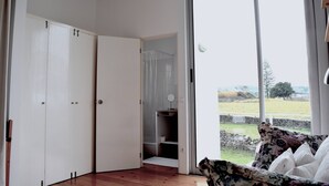 Una habitación con un gran ventanal corredero que da a un balcón, un armario blanco y un baño pequeño con ducha.