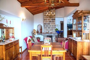 A dining area with a wooden table and chairs, a stone fireplace, and wooden cabinets. - QUINTA DAS BOLAS by Azores HomeMade (Ponta Delgada)