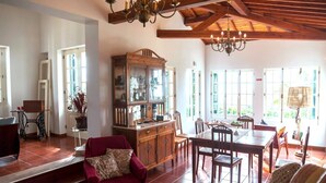 A spacious room with a dining table, chairs, a red armchair, a wooden cabinet, and a chandelier. - QUINTA DAS BOLAS by Azores HomeMade (Ponta Delgada)