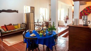 A dining area with a blue tablecloth, chairs, and a variety of food and drinks. There is a sofa with cushions in the background and a chandelier above the table. - QUINTA DAS BOLAS by Azores HomeMade (Ponta Delgada)