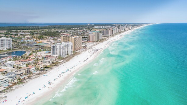 Un paysage urbain côtier avec une longue plage de sable, de grands hôtels et une mer bleue et limpide.