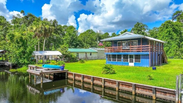 A lakeside cabin with a dock, a small boat, and a grassy area with a building. - Charming 2-bedroom LAKEHOUSE house with WiFi, AC on George's Lake! (Florahome)