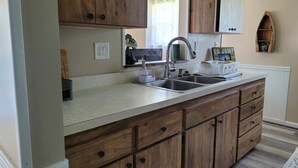 A kitchen with wooden cabinets, a double sink, and a countertop with a toaster. - Charming 2-bedroom LAKEHOUSE house with WiFi, AC on George's Lake! (Florahome)