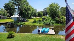 A serene lakeside view with a dock, a small boat, and an American flag. - Charming 2-bedroom LAKEHOUSE house with WiFi, AC on George's Lake! (Florahome)