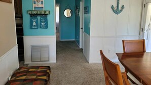 A kitchen with teal walls, a wooden dining table, and a patterned bench. - Charming 2-bedroom LAKEHOUSE house with WiFi, AC on George's Lake! (Florahome)