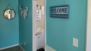 A teal-walled hallway with a welcome sign, a mirror, and a decorative wall piece. - Charming 2-bedroom LAKEHOUSE house with WiFi, AC on George's Lake! (Florahome)