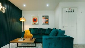 Una sala de estar moderna con un sofá color turquesa, una mesa de centro y una lámpara. Hay dos carteles enmarcados en la pared y un letrero de neón.