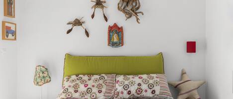 A bedroom with a green headboard, floral bedding, and wall art including a cat, octopus, and a religious icon.