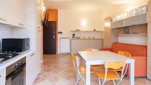 A compact kitchen with a stove, microwave, and oven. There is a dining table with orange chairs and a sofa. - Relax in Loano With Terrace by Wonderful Italy (Loano)