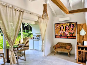 A room with a dining area, a sofa, a painting, and a kitchen visible through an open door. - The White Palm - Tropical Bungalow (Sainte Rose)