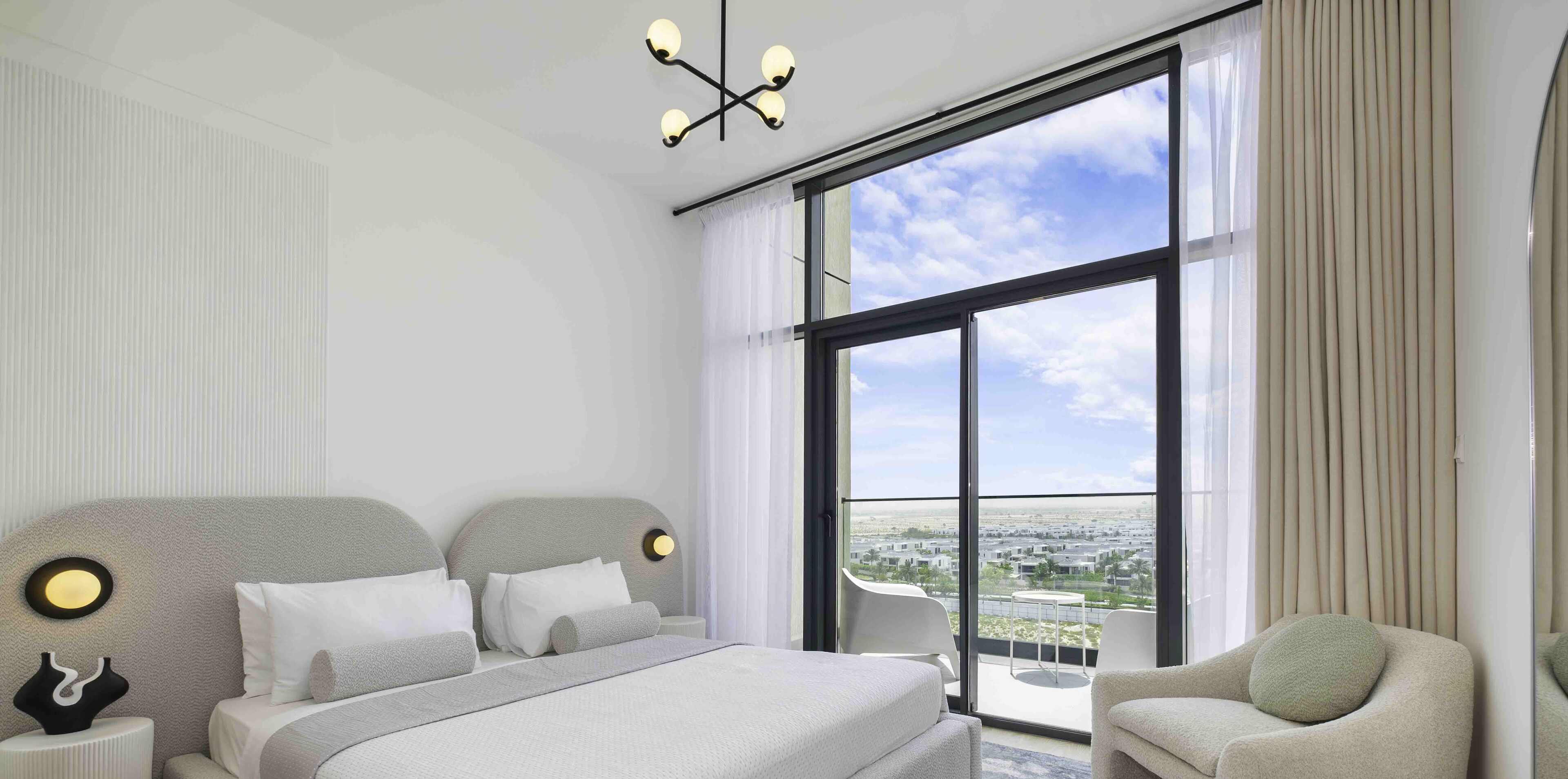 A modern hotel room with a large bed, a sitting area, and a balcony with a city view.