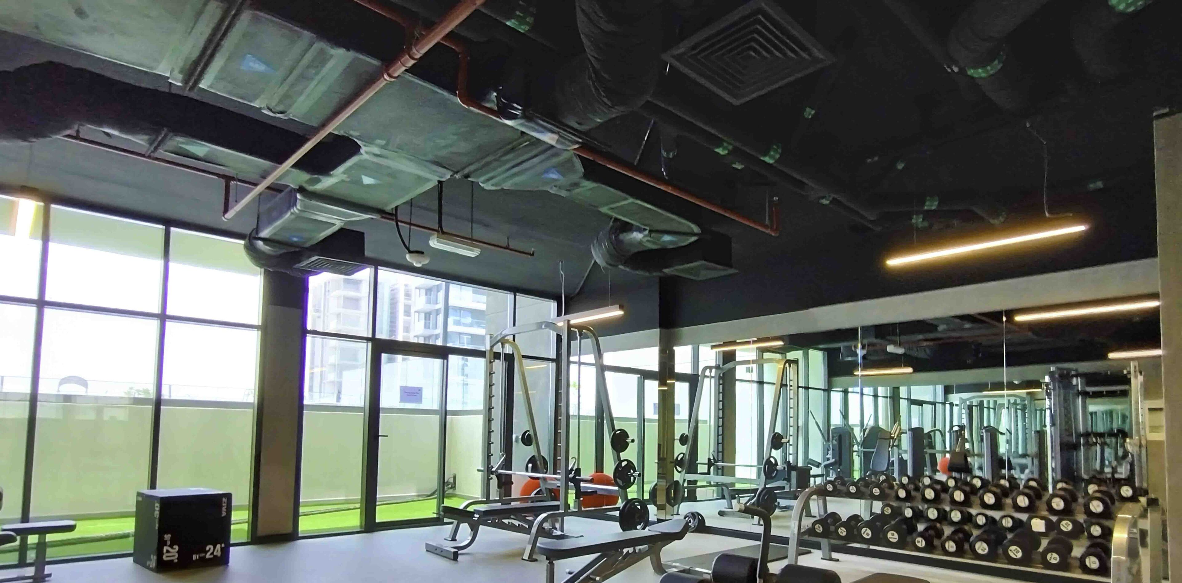 A gym with weightlifting equipment, mirrors, and large windows.