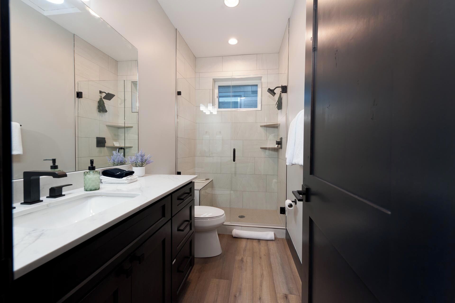 A modern bathroom with a large mirror, a white sink, a toilet, and a shower area.