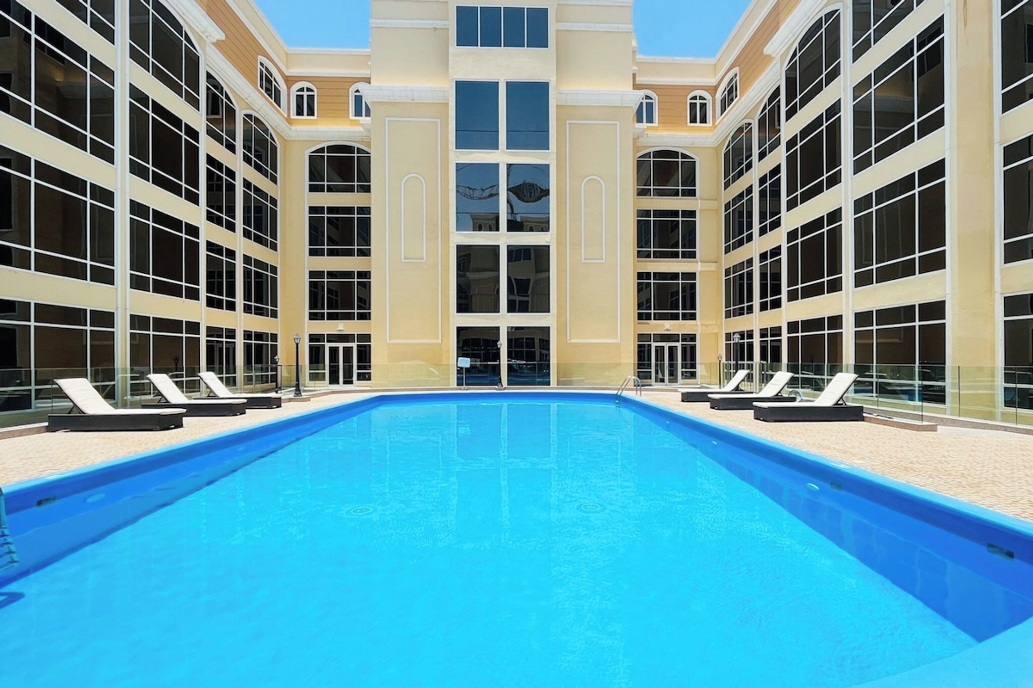 A swimming pool with lounge chairs and a building with large windows and a central entrance.