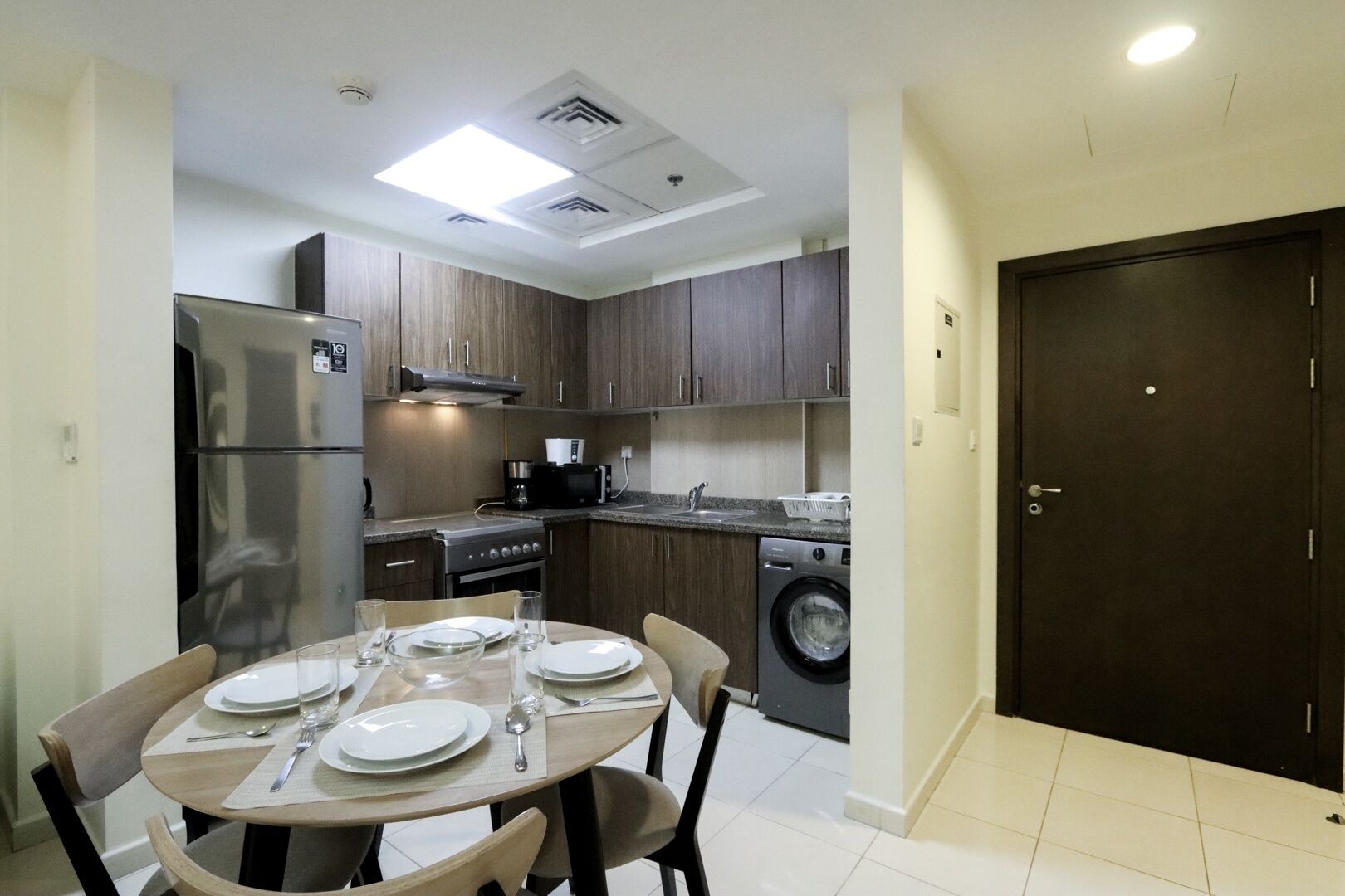 Una cocina compacta con electrodomésticos modernos, un comedor con una mesa redonda y una puerta oscura.
