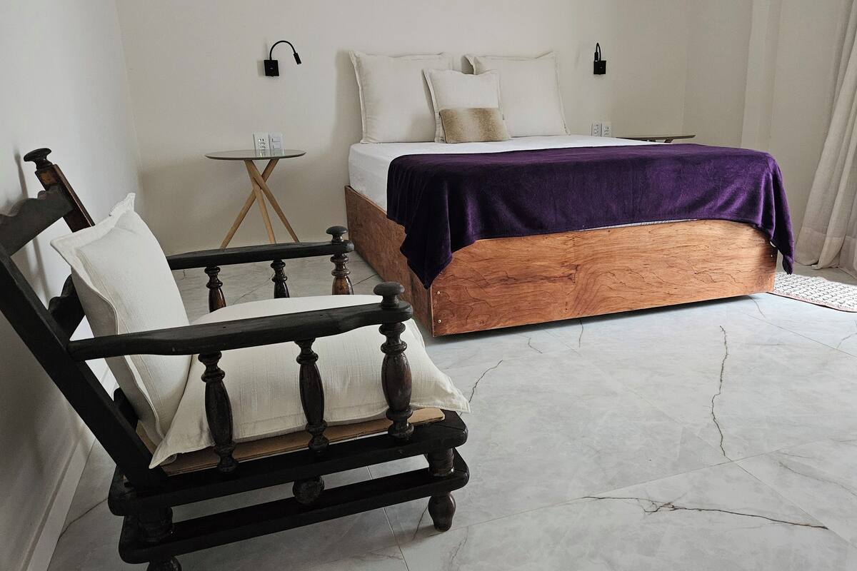 A bedroom with a wooden bed, a wooden chair, a small table, and a white wall.