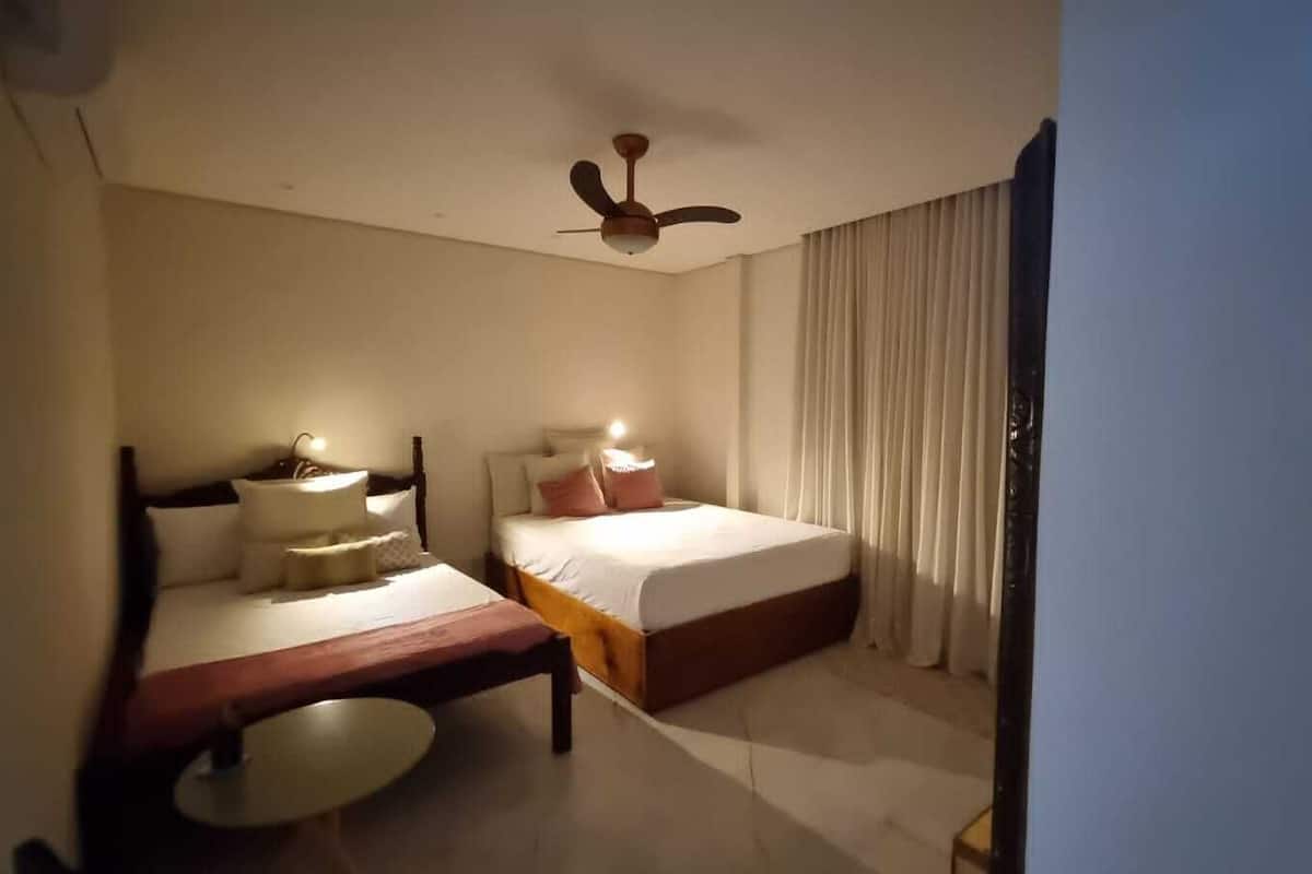 A hotel room with two beds, a ceiling fan, and a bedside table with a lamp.