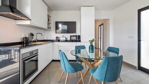 Une cuisine moderne avec des meubles blancs, une hotte noire et une table à manger en verre, accompagnée de quatre chaises bleues.