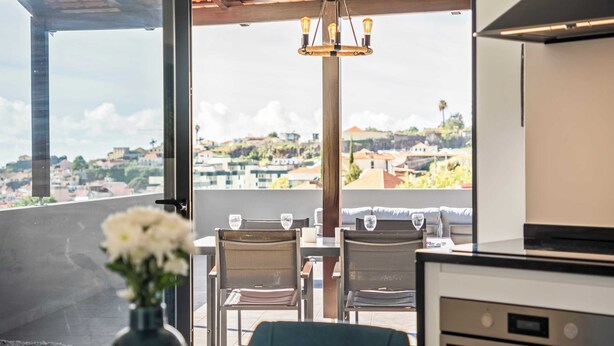 Un coin repas avec une table dressée pour deux personnes, un vase rempli de fleurs et une vue sur une colline.
