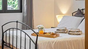 Un lit bien fait, sur lequel est posé un plateau contenant divers éléments pour le petit-déjeuner, notamment un panier de fruits, un verre de jus d’orange et un croissant.