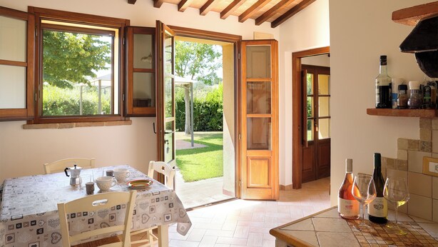 A kitchen with a dining table, chairs, and a view of the garden through open doors.