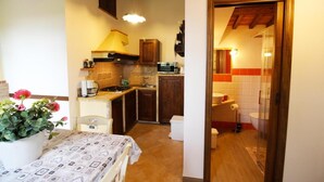 A compact kitchen with wooden cabinets, a stove, and a microwave. There's a dining table with a patterned tablecloth and a potted plant.