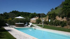 A swimming pool with lounge chairs and a hot tub, surrounded by greenery and hills.