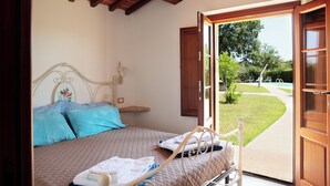 A bedroom with a bed, a bedside table, and a view of a garden and pool.