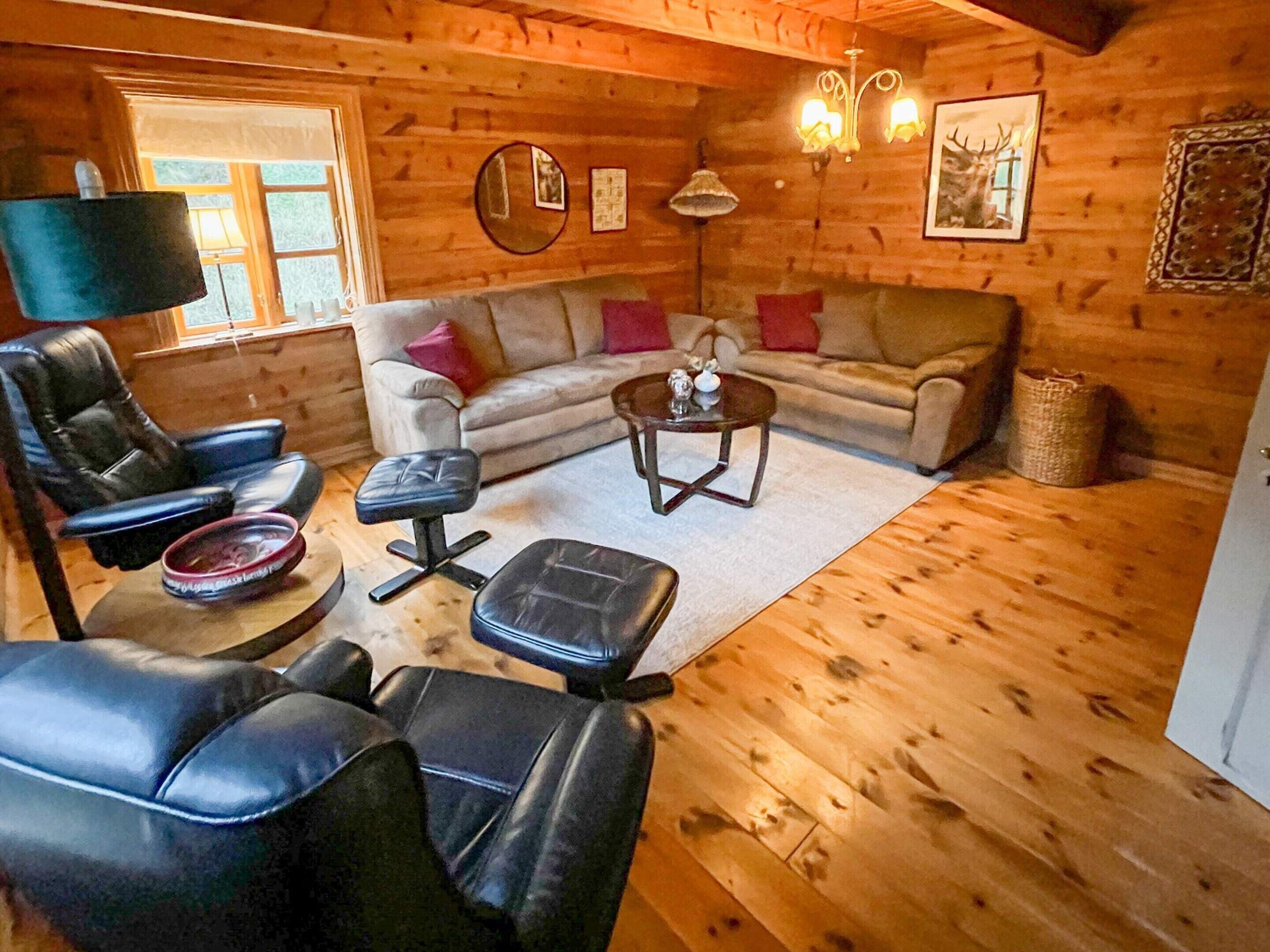 Acogedor interior de una cabaña de madera con un sofá de cuero, una mesa de centro y un sillón de cuero.