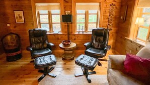 Ein gemütliches Blockhaus-Interieur mit zwei Ledersesseln, einem kleinen runden Tisch und einer Couch.