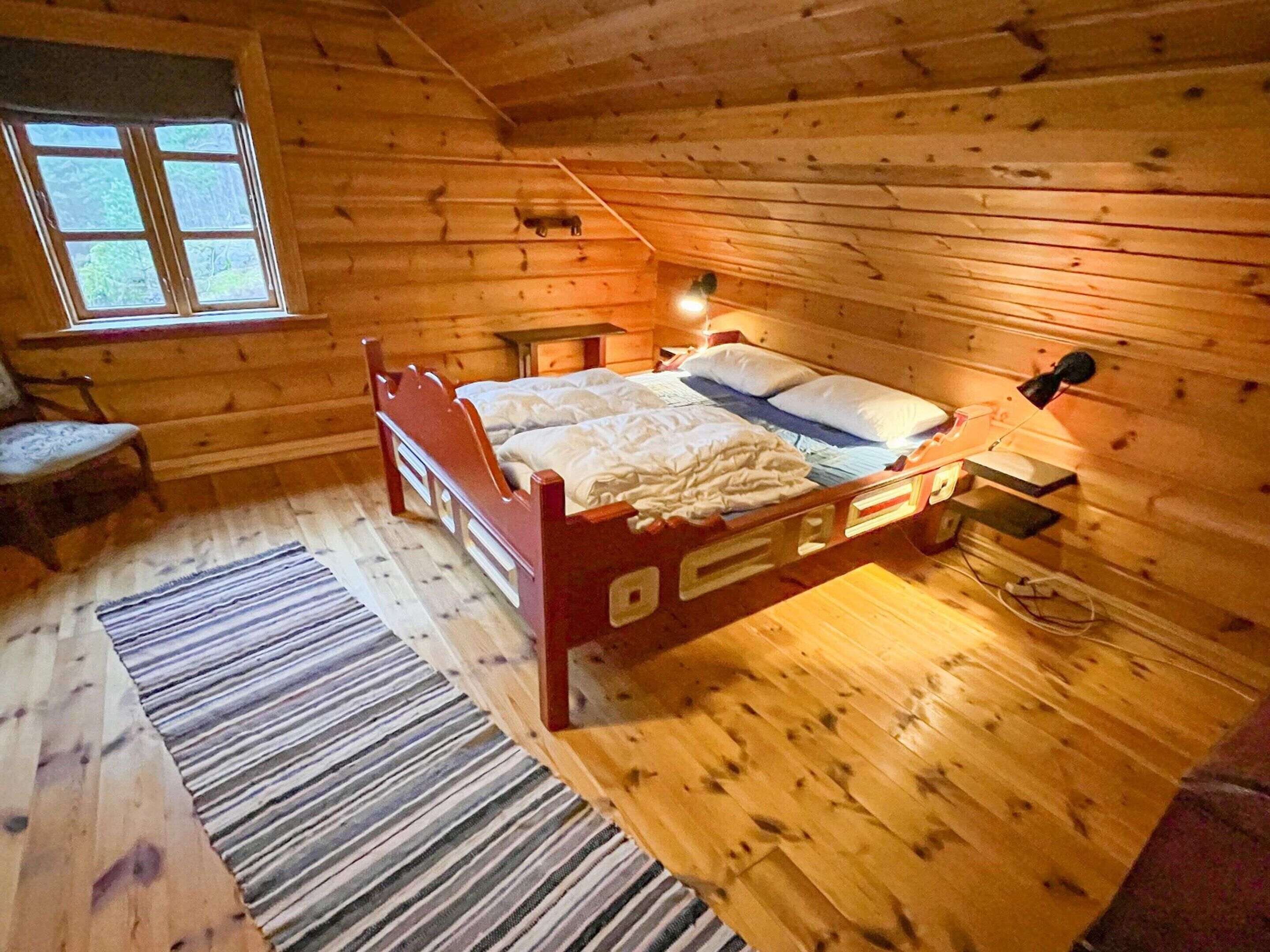 A wooden cabin bedroom with a bed, a nightstand, a lamp, and a window.