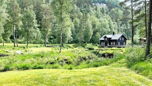 Ein Haus, umgeben von einer üppigen, grünen Landschaft mit Teich und dichten Bäumen.