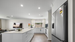 A modern kitchen with white cabinetry, a stainless steel refrigerator, and a central island. - Air Conditioning *  Secured Parking * BBQ * No Linen (South West Rocks)