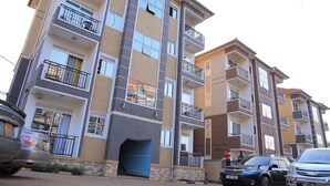 A multi-story residential building with balconies, a blue entrance, and parked cars. - Najjera, Kampala 1bed With Balcony, Wifi & Parking (Kampala)