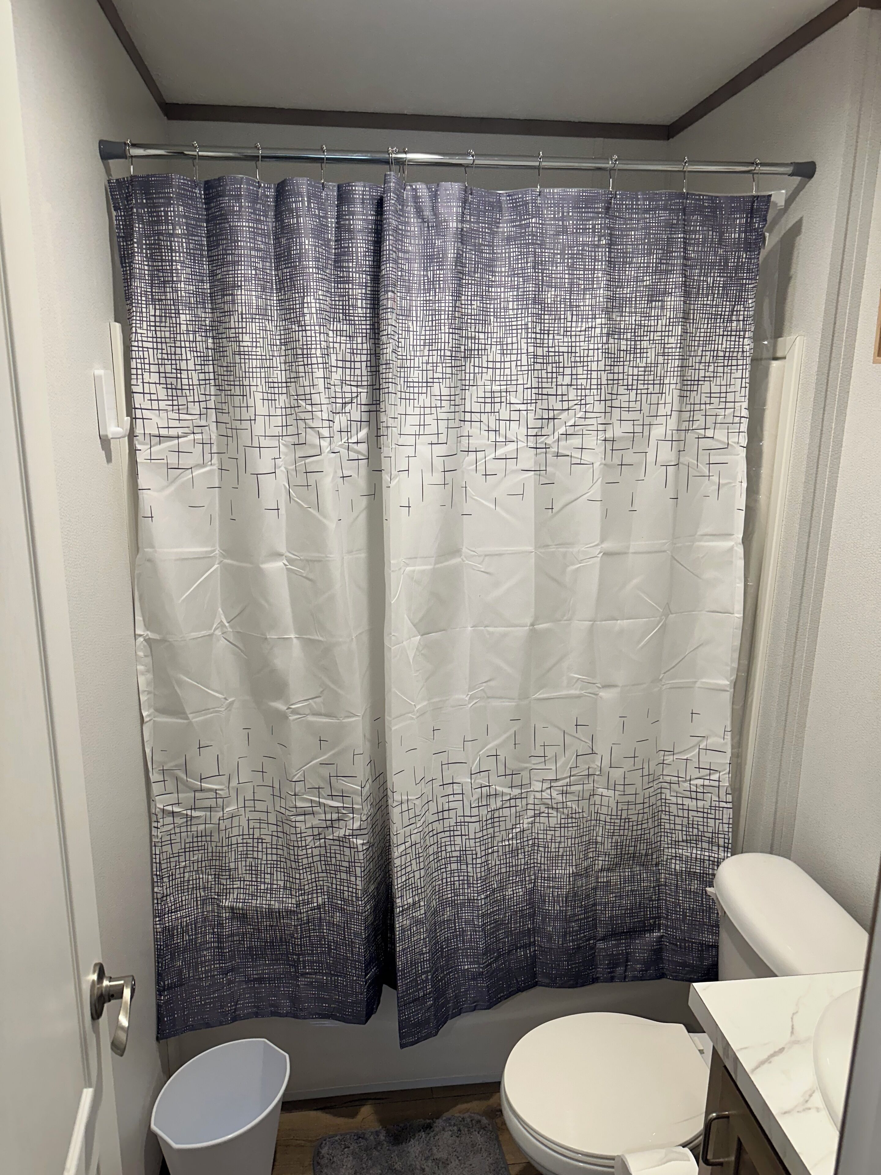 Ein Badezimmer mit Duschvorhang mit geometrischem Muster, Toilette und Waschbecken mit Marmorplatte.