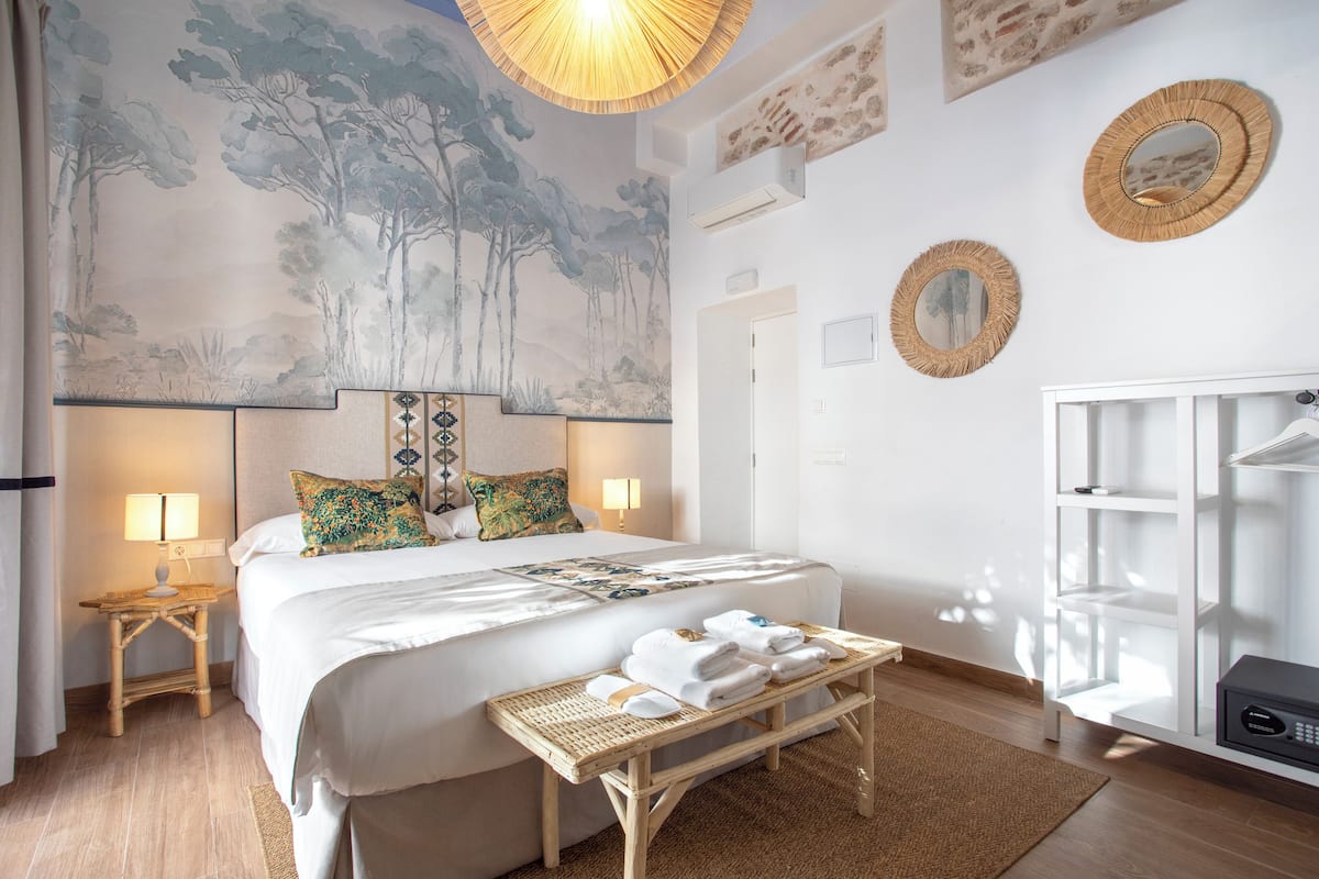 Habitación de hotel con una cama grande, dos lámparas de noche, aire acondicionado de pared, un espejo y un armario blanco.
