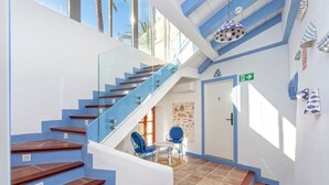 Una escalera moderna con barandillas de cristal y peldaños de madera, que conduce a una habitación con pared de piedra y una puerta señalizada con una flecha.