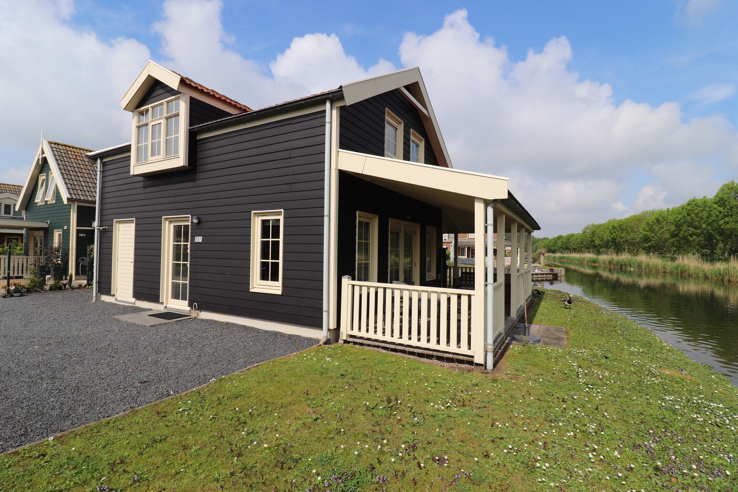 A two-story house with a porch, a small pond, and a grassy area with flowers.