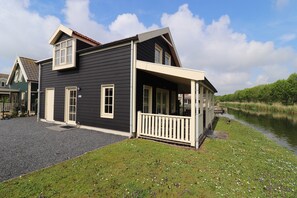 A two-story house with a porch, a small pond, and a grassy area with flowers. - Sun-soaked Bungalow in Simonshaven (Simonshaven)