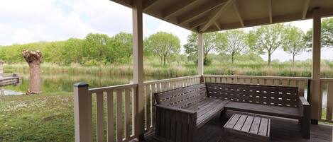 A covered outdoor seating area with a bench and a table, overlooking a natural landscape with trees and a body of water.