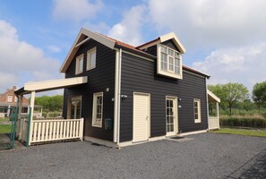 A two-story house with a porch, a fenced yard, and a gravel driveway. - Sun-soaked Bungalow in Simonshaven (Simonshaven)