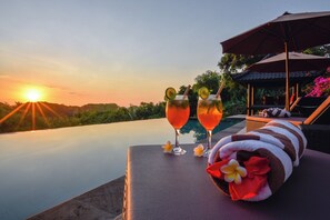 Blick auf den Sonnenuntergang von einem Poolbereich mit zwei Cocktails und einem Handtuch.