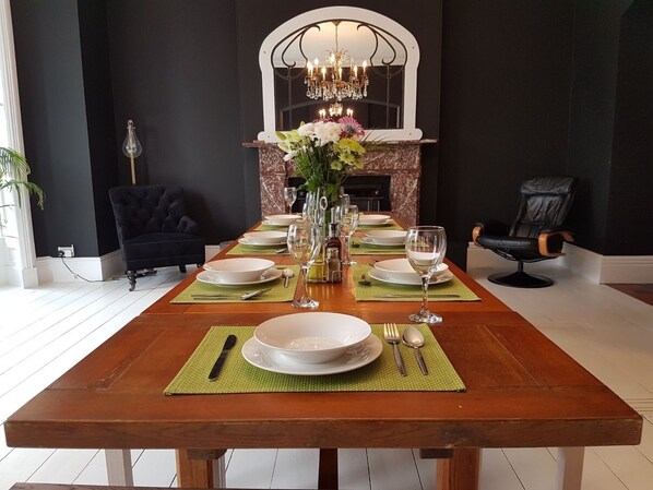 A dining table set with plates, glasses, and cutlery, flanked by chairs and a sofa, with a fireplace and chandelier in the background. - Beautiful Pendine Manor House in West Wales (Carmarthen)